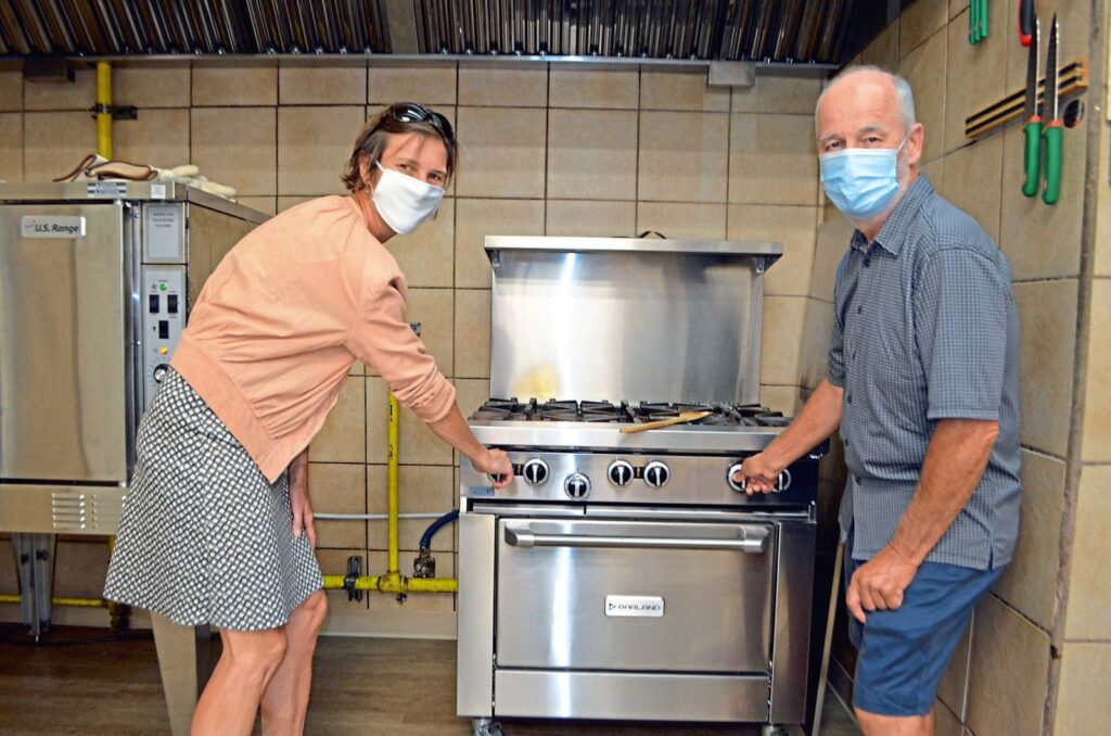 Two people in masks pose in front of a gas burning stove.